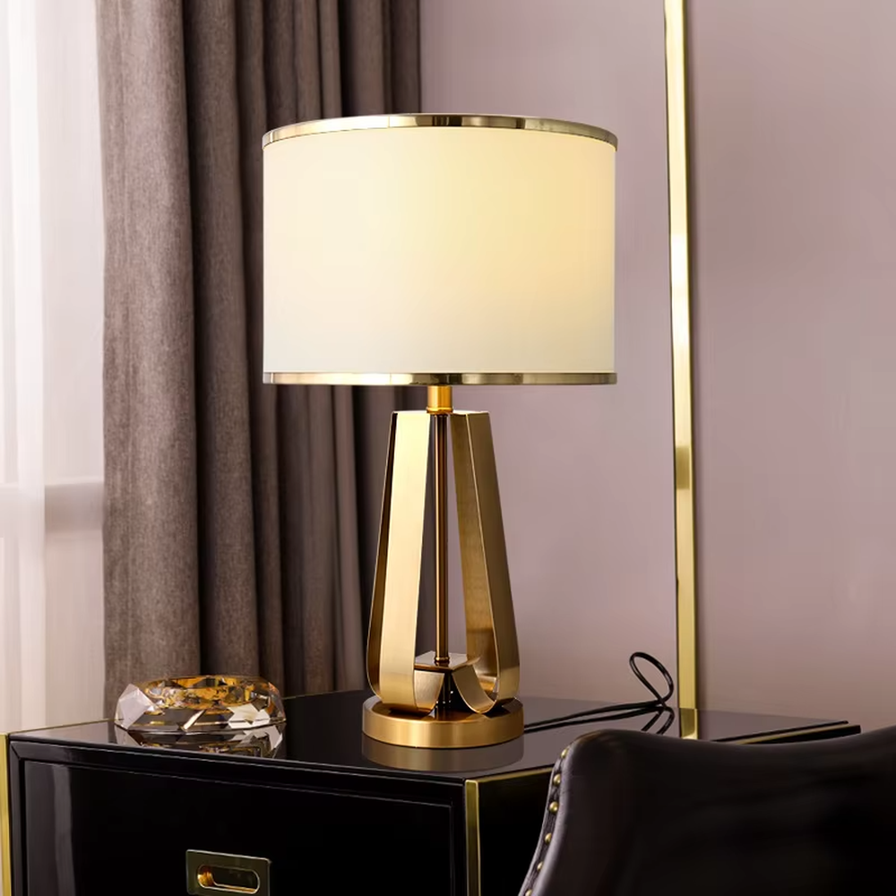 This is a light luxury geometric metal table lamp, featuring a gold polygonal hollow lamp base paired with an off-white fabric lampshade (with gold trim). It emits soft and warm light, serving both lighting and decorative purposes, suitable for bedroom nightstands, light luxury living room side tables, hotel guest rooms, showrooms and other scenarios.