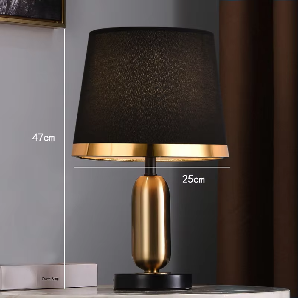This is a light luxury minimalist style table lamp, featuring a gold metal lamp body paired with an off-white fabric lampshade. The black and gold color scheme offers a high-end texture, emitting soft and uniform light, serving both lighting and decorative purposes, suitable for bedroom nightstands, hotel guest rooms, light luxury living room side tables and other scenarios.