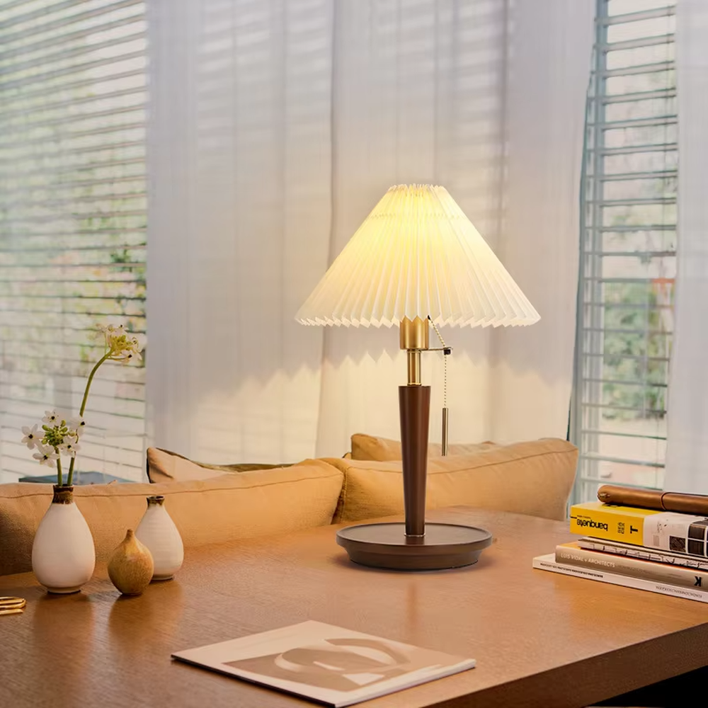Vintage Nordic pleated fabric table lamp, with an off-white pleated fabric lampshade paired with a dark brown wood and gold metal spliced lamp pole, featuring a pull-cord switch, emitting soft and warm light, combining decorativeness and practicality, suitable for lighting and decoration in spaces such as bedroom nightstands, living room side tables, and B&B guest rooms.