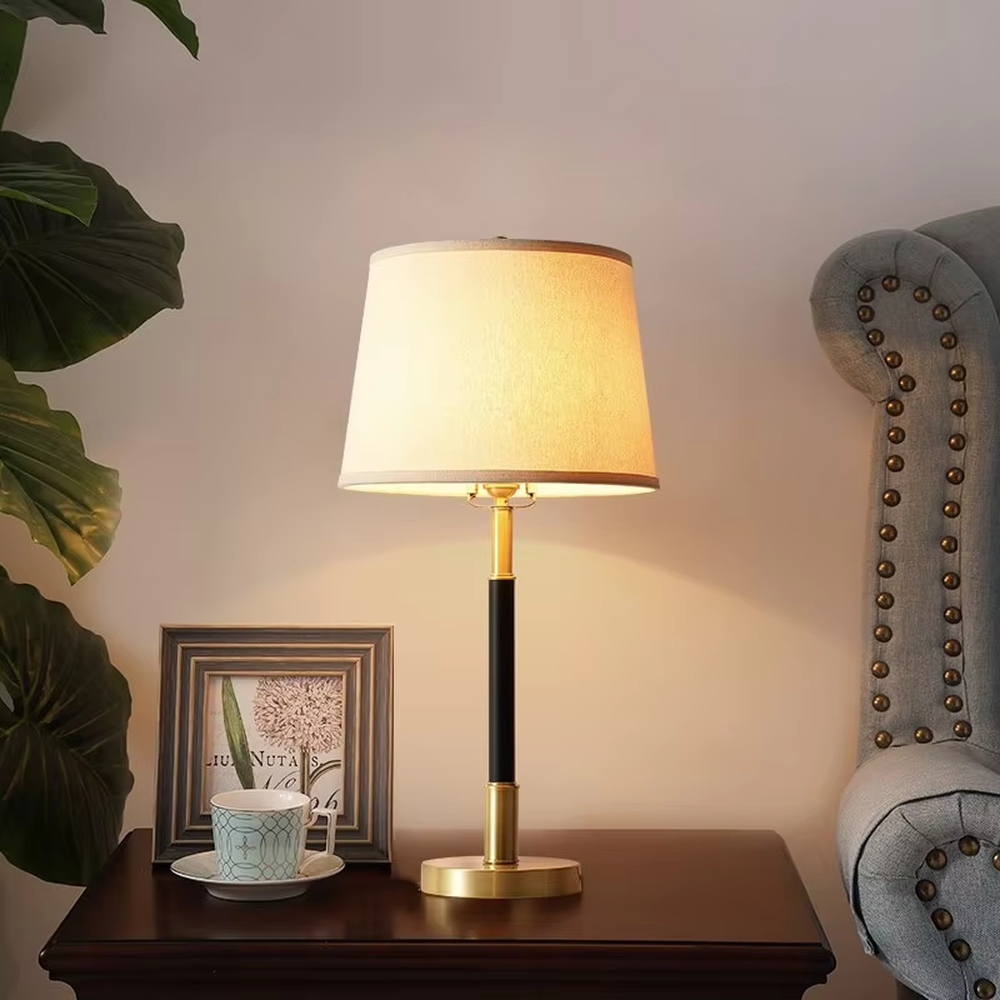 This table lamp features a black and gold contrasting metal lamp pole paired with an off-white fabric lampshade, with a glossy gold metal base. It presents a style that combines modern light luxury and minimalist retro, with soft eye-protective light, serving both lighting and decorative purposes, suitable for placement in bedrooms, studies and other spaces.