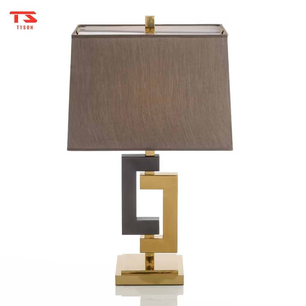 This is a modern light luxury geometric interlocking table lamp, featuring an interlocking geometric lamp body crafted from gold and gray dual-color metal, paired with a dark gray fabric lampshade. It emits soft and uniform light, serving both lighting and decorative purposes, suitable for bedroom nightstands, light luxury living room side tables, hotel guest rooms, showrooms and other scenarios.