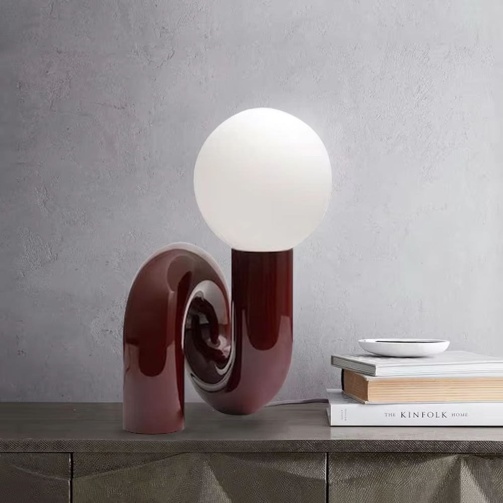 This art table lamp features a spiral S-shaped stand made of glossy wine-red material, paired with a milky white spherical lampshade, with a vivid and retro shape, serving both lighting and decorative purposes, ideal for bedrooms, living rooms, internet-famous shops and other spaces.