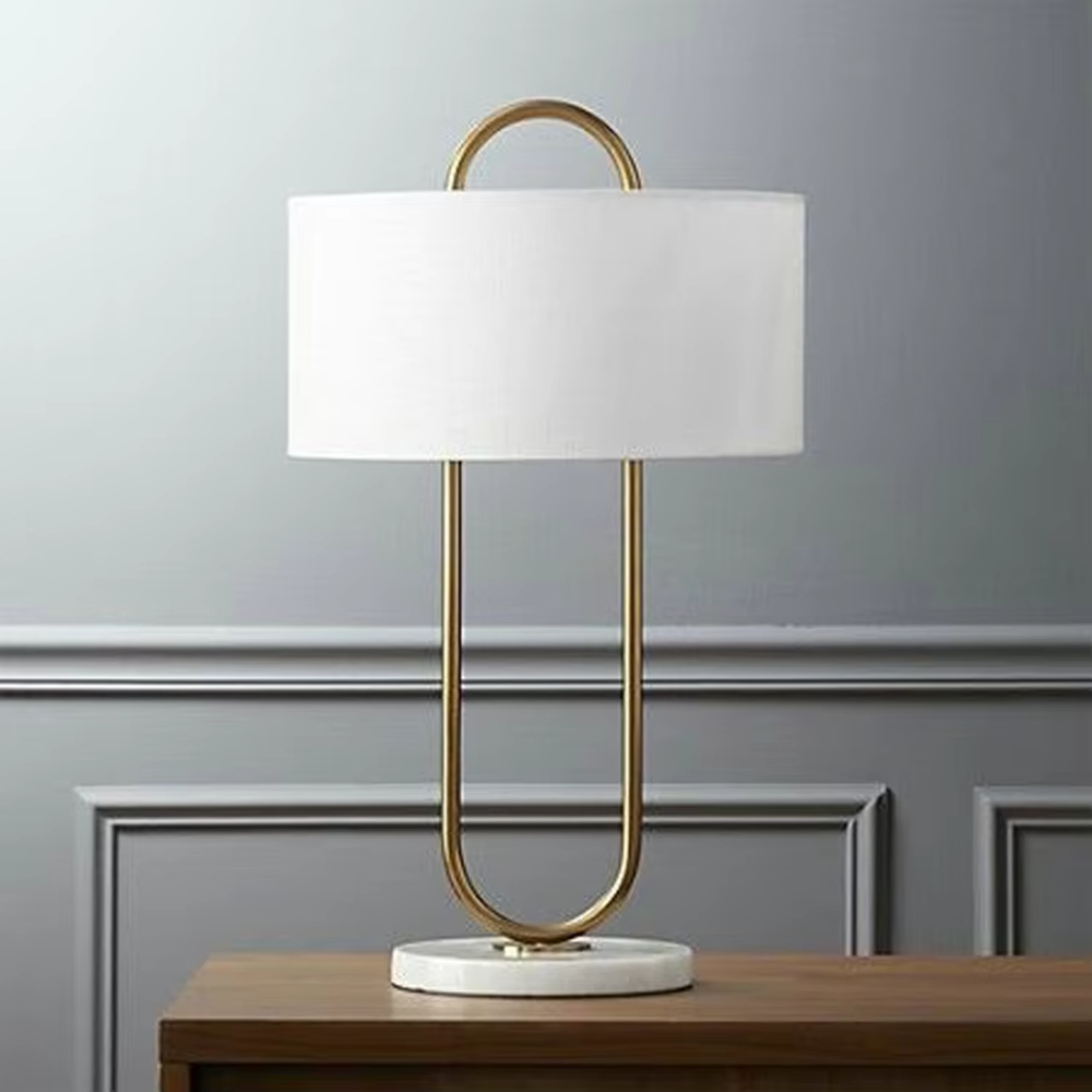 This modern light luxury table lamp features a U-shaped frame made of gold metal, paired with a white fabric rectangular lampshade and a white marble base, with a simple and elegant shape. It serves both lighting and decorative purposes, ideal for light luxury spaces such as bedroom bedside tables, living room side tables, and hotel guest rooms.
