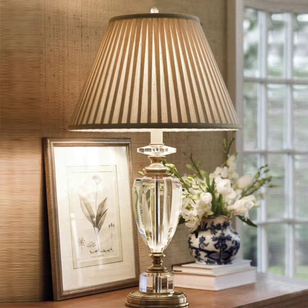 Light luxury crystal table lamp, with a transparent cut crystal column base, gold metal details and a beige pleated fabric lampshade for soft and eye-protective lighting, designed to enhance the elegant atmosphere of spaces, suitable for bedroom nightstands, living room side tables, hotel guest rooms, etc.