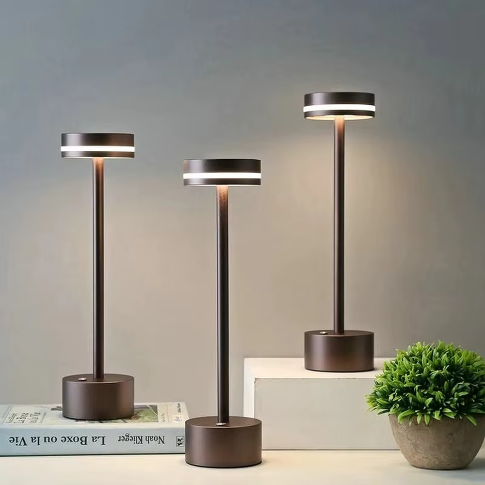 Modern minimalist bronze metal rechargeable table lamp, featuring a cylindrical lamp body and a top ring-shaped lighting design, emitting soft and even light. It supports wireless battery life and touch dimming, suitable for ambient lighting and supplementary lighting in scenarios such as dining tables, bars, and bedroom nightstands.