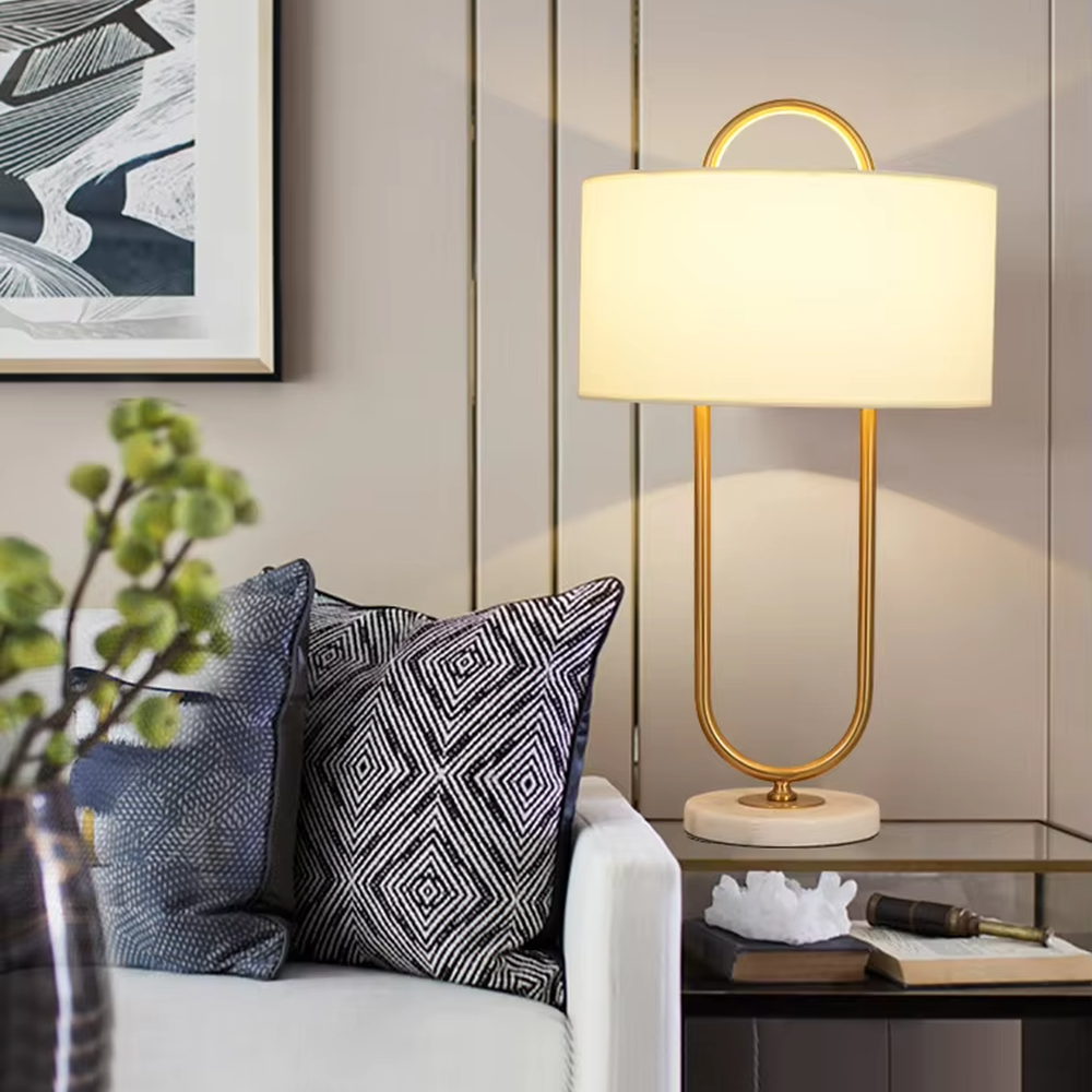 This modern light luxury table lamp features a U-shaped frame made of gold metal, paired with a white fabric rectangular lampshade and a white marble base, with a simple and elegant shape. It serves both lighting and decorative purposes, ideal for light luxury spaces such as bedroom bedside tables, living room side tables, and hotel guest rooms.