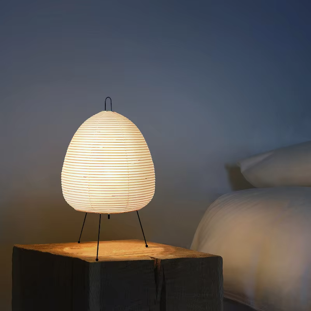 This wabi-sabi style egg-shaped table lamp features a striped light-transmitting paper lampshade, supported by a black metal tripod, with a simple and soft shape, serving both lighting and decorative purposes, ideal for bedroom bedside tables, homestay rooms, wabi-sabi style spaces and other scenarios.