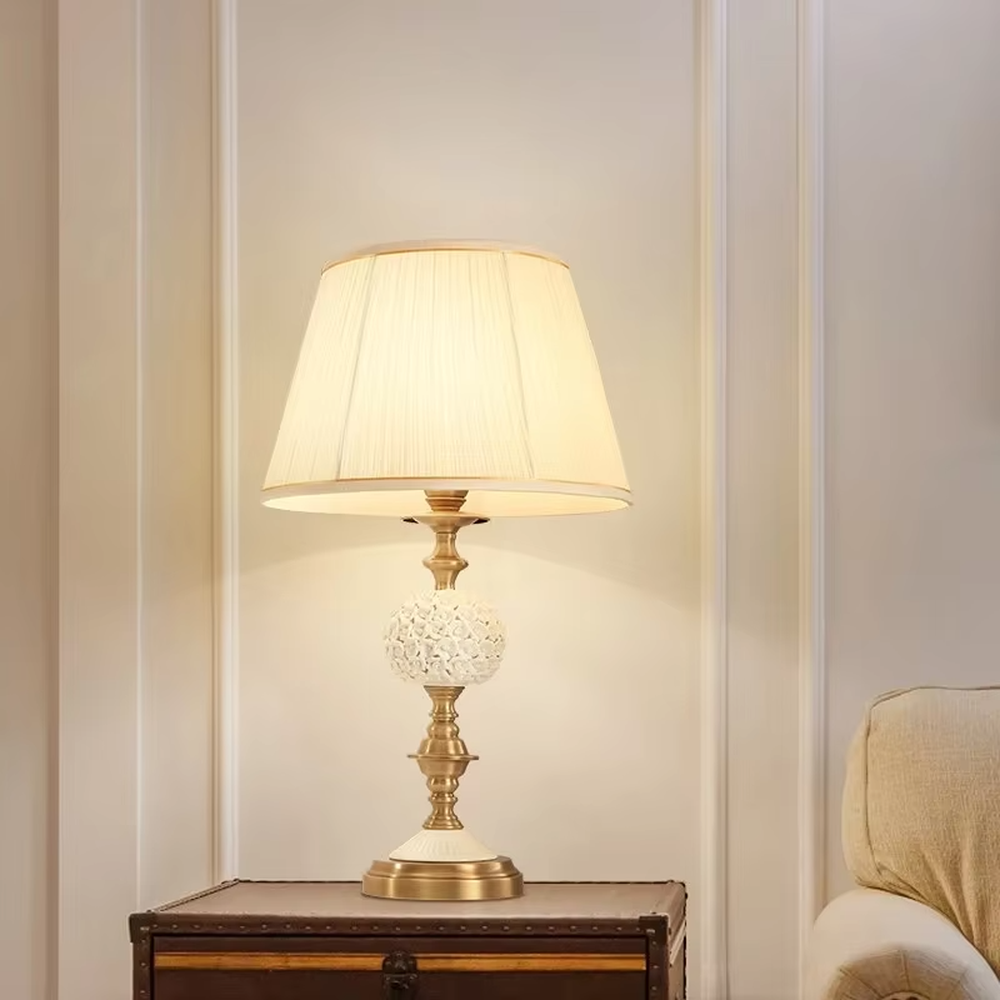 This European light luxury table lamp features a glossy gold metal base, paired with hollow carved crystal decorations and an off-white pleated fabric lampshade, presenting a luxurious and retro court texture. The light is soft and warm, serving both lighting and decorative purposes, suitable for placement in European-style spaces such as bedrooms and villa guest rooms.
