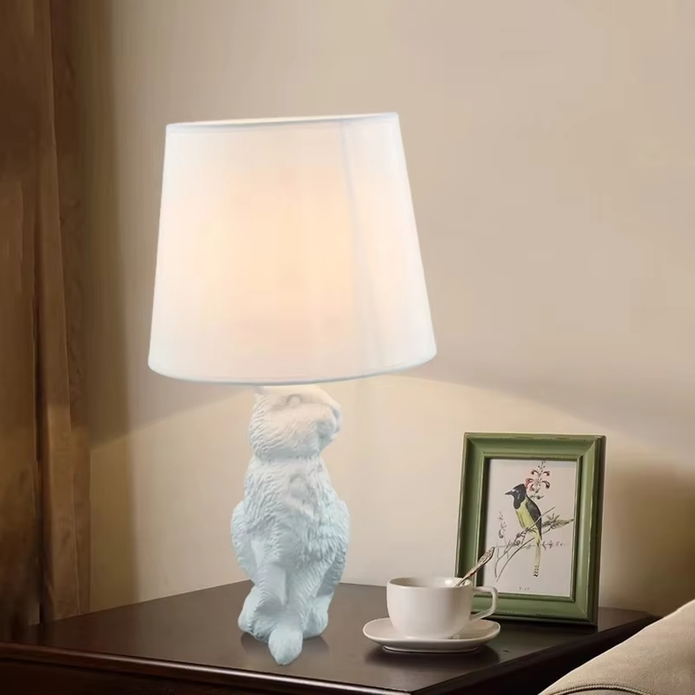 This dark art style table lamp features a bionic rabbit-shaped base made of black resin, paired with a black fabric cylindrical lampshade. The rabbit-lifting-lampshade design is full of fantasy, serving both lighting and decorative purposes, ideal for trendy toy spaces, personalized homes, internet-famous shops and other scenarios.