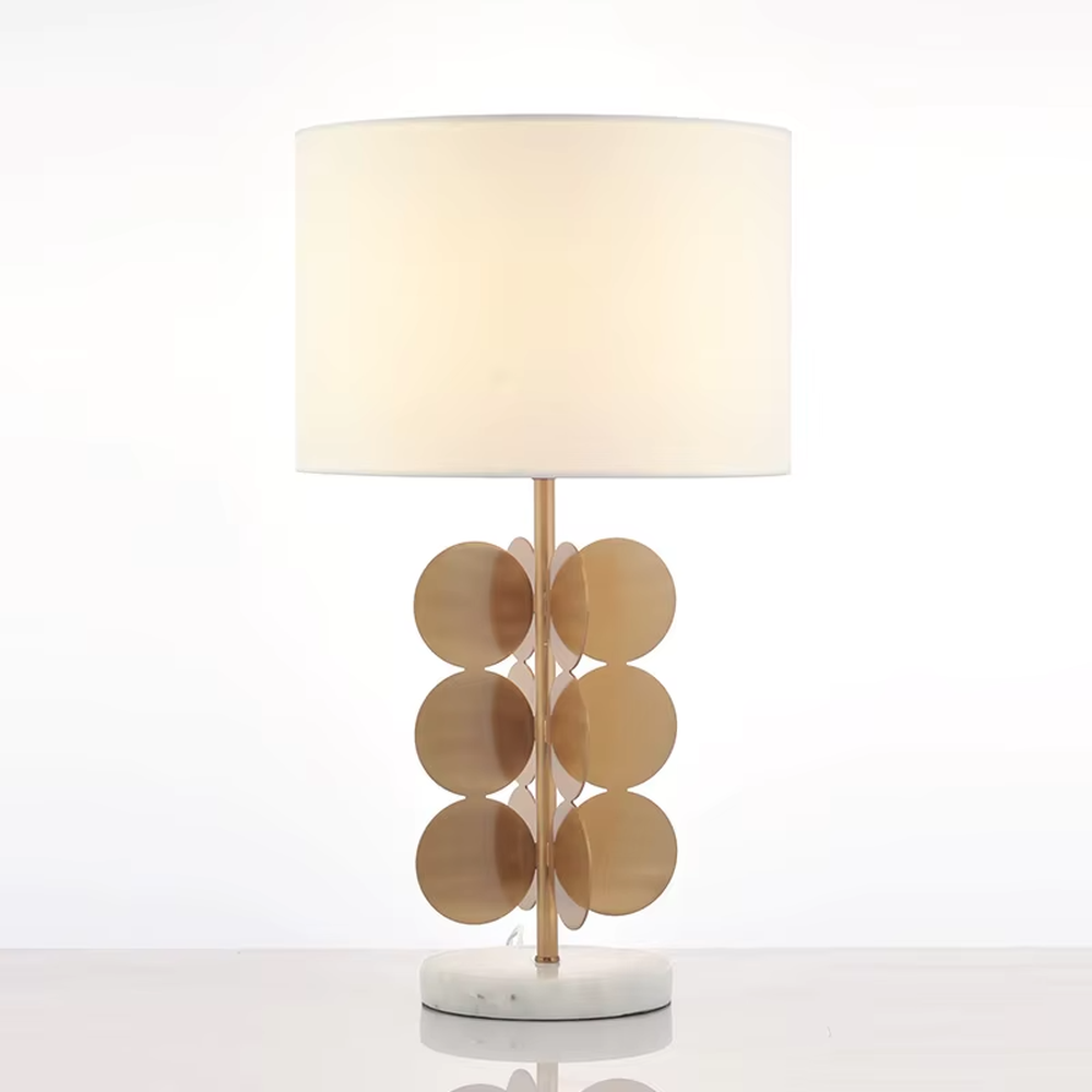 This light luxury table lamp features a white fabric cylindrical lampshade on top, a lamp post with a staggered stack of gold metal discs, and a white marble base, serving both lighting and decorative purposes, ideal for living room side tables, bedroom bedside tables, light luxury homestays and other spaces.