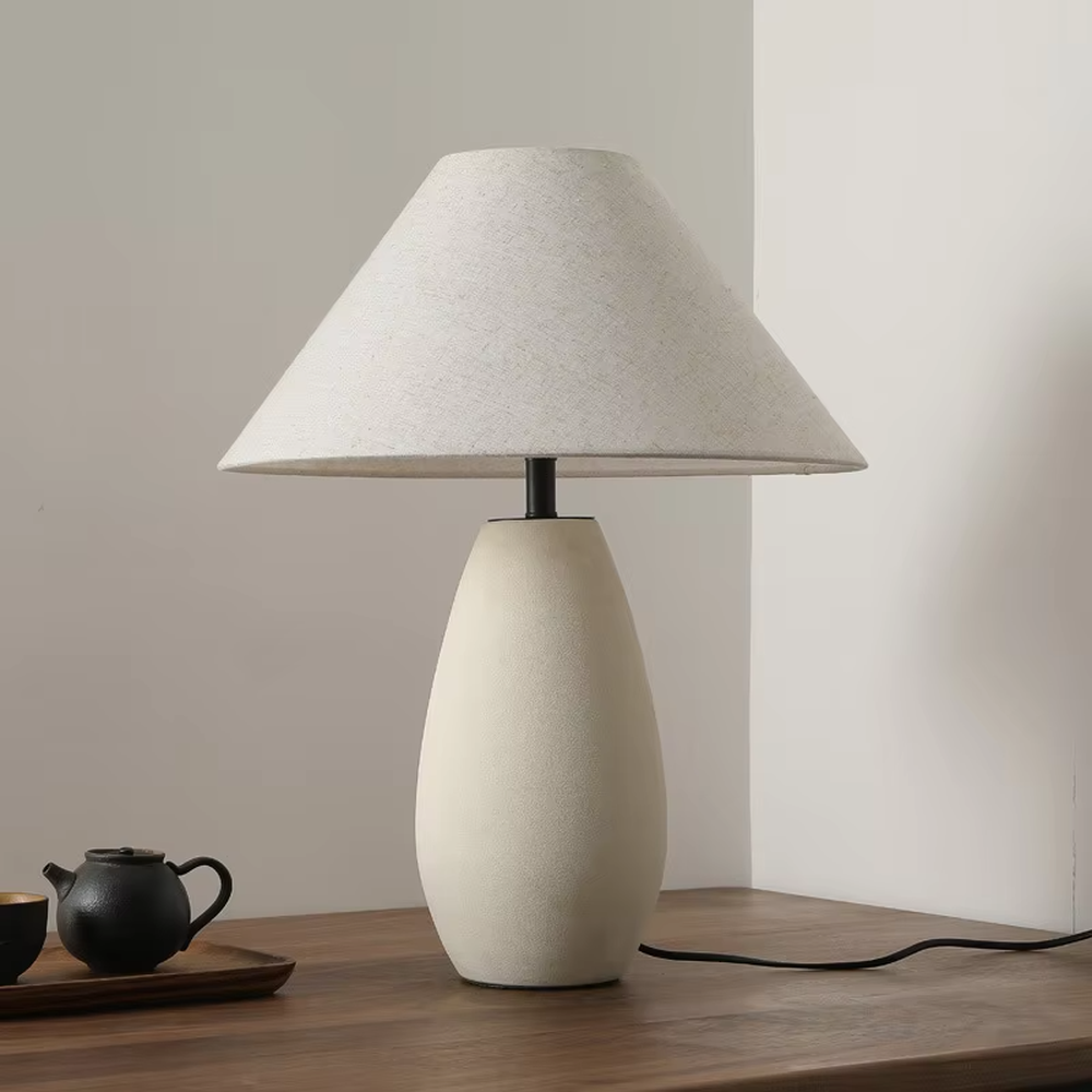 This is a wabi-sabi style minimalist table lamp, featuring an off-white frosted ceramic base paired with a linen fabric lampshade. The light is soft and warm, serving both lighting and decorative purposes, suitable for scenarios pursuing a warm and relaxed feeling such as bedroom nightstands, homestay guest rooms, Japanese-style tea rooms, and wabi-sabi style living rooms.