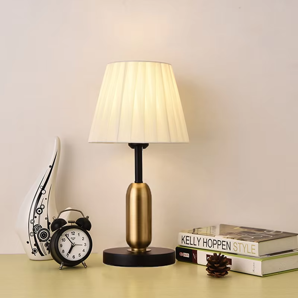 This is a light luxury minimalist style table lamp, featuring a gold metal lamp body paired with an off-white fabric lampshade. The black and gold color scheme offers a high-end texture, emitting soft and uniform light, serving both lighting and decorative purposes, suitable for bedroom nightstands, hotel guest rooms, light luxury living room side tables and other scenarios.