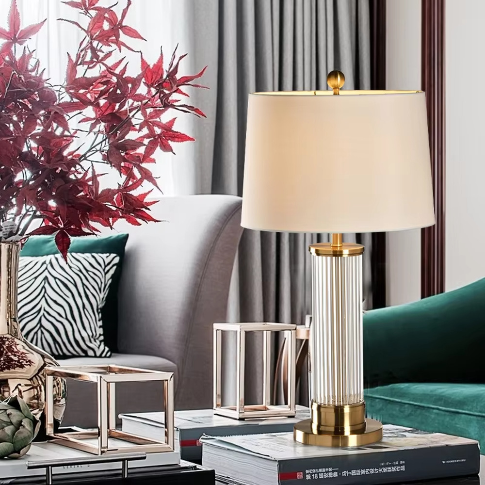 This is a light luxury crystal metal table lamp, with an off-white fabric lampshade edged with gold trim, a lamp post made of vertical striped transparent crystal paired with gold metal splicing, and a gold metal base, featuring both decorative and lighting functions, ideal for high-end indoor scenarios such as bedroom nightstands and living room side tables.