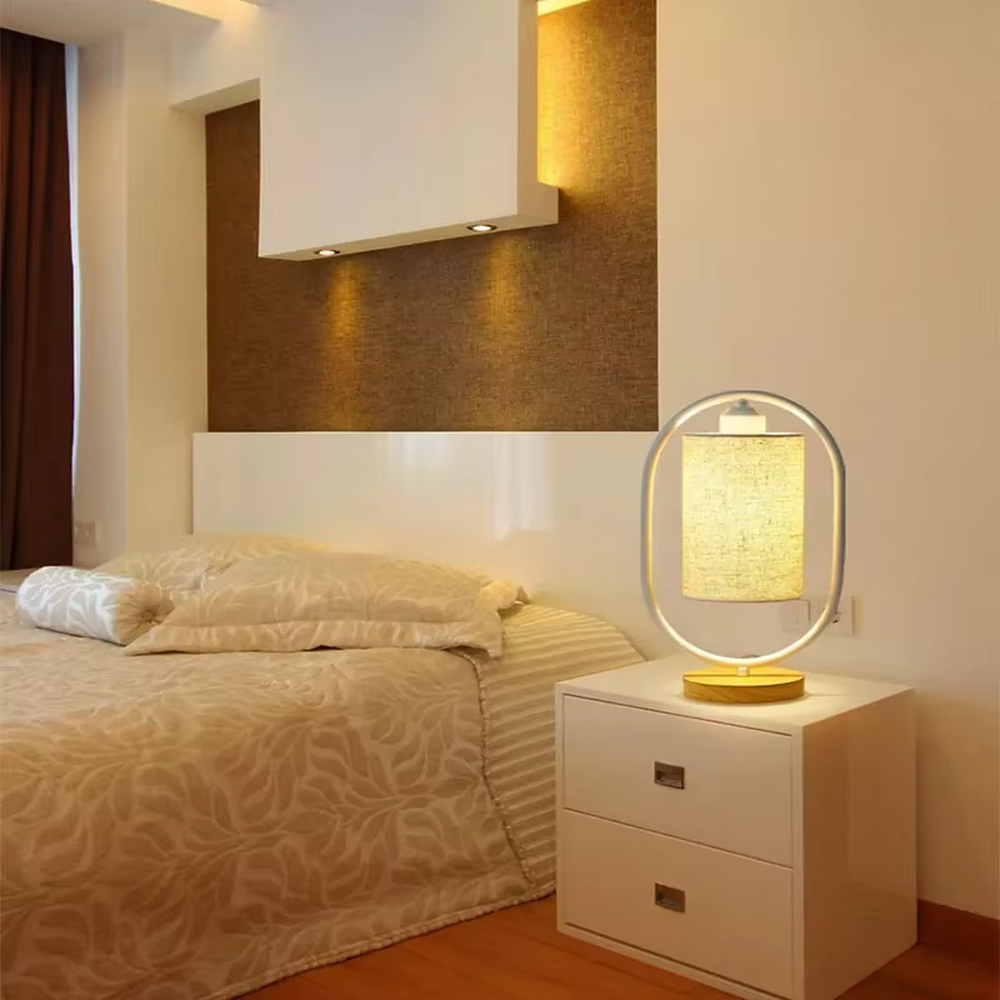 Modern minimalist silver oval metal frame linen texture lampshade wooden base table lamp, warm light effect, creating a cozy minimalist home atmosphere.