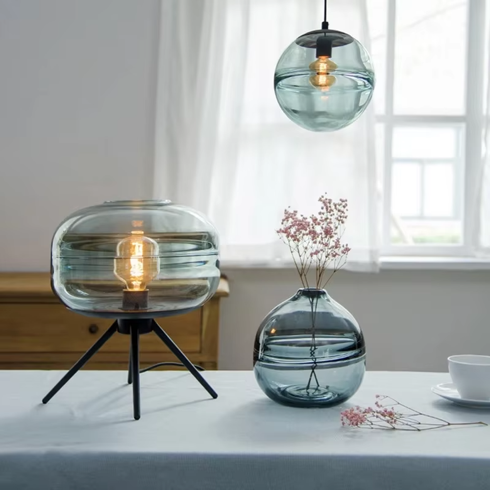 This set of Nordic-style glass lighting includes a table lamp and a chandelier, with drum-shaped lampshades made of blue-gray gradient glass. The table lamp is paired with a black tripod base, and the chandelier uses a suspension design, emitting soft and transparent light, serving both lighting and decorative purposes, ideal for bedrooms, dining rooms, Nordic-style homes and internet-famous shops and other scenarios.