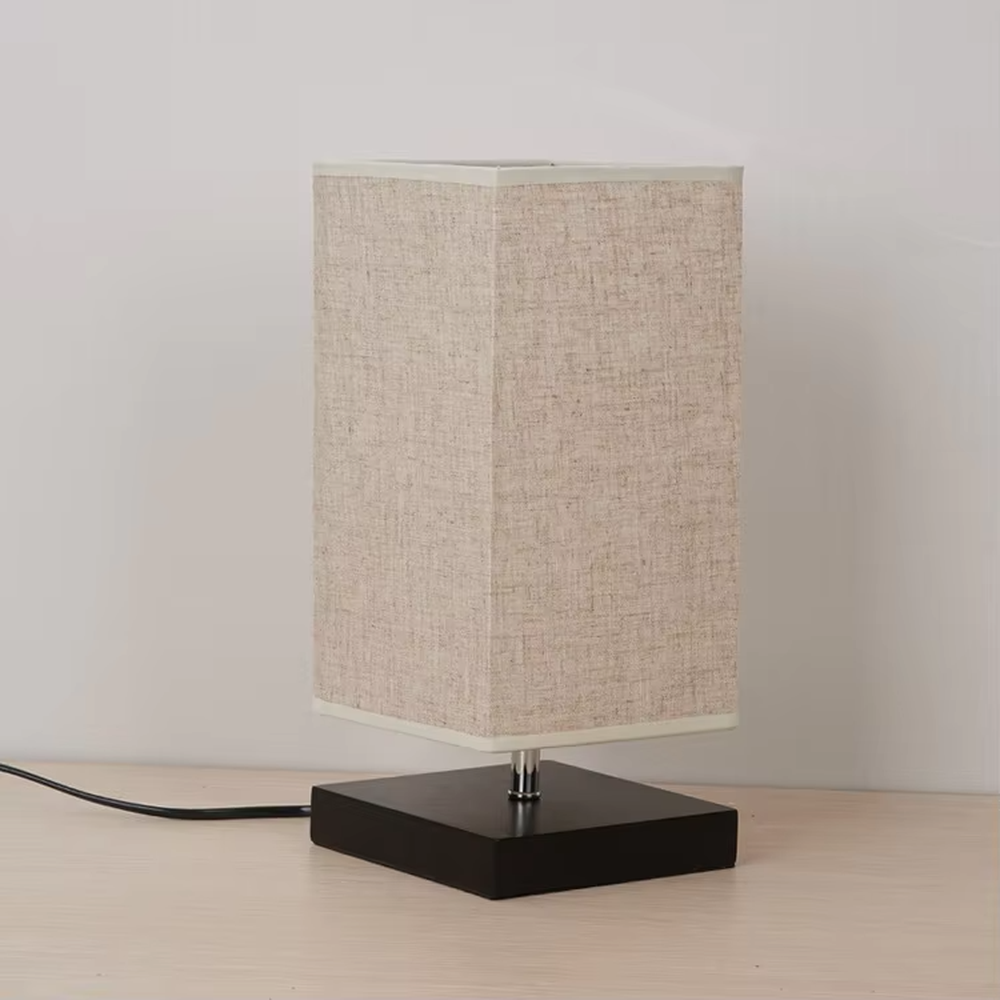 This is a minimalist square fabric table lamp, featuring a light beige linen lampshade paired with a black solid wood base. It emits soft and warm light, serving both lighting and decorative purposes, suitable for bedroom nightstands, desks, homestay guest rooms, living room side tables and other scenarios.