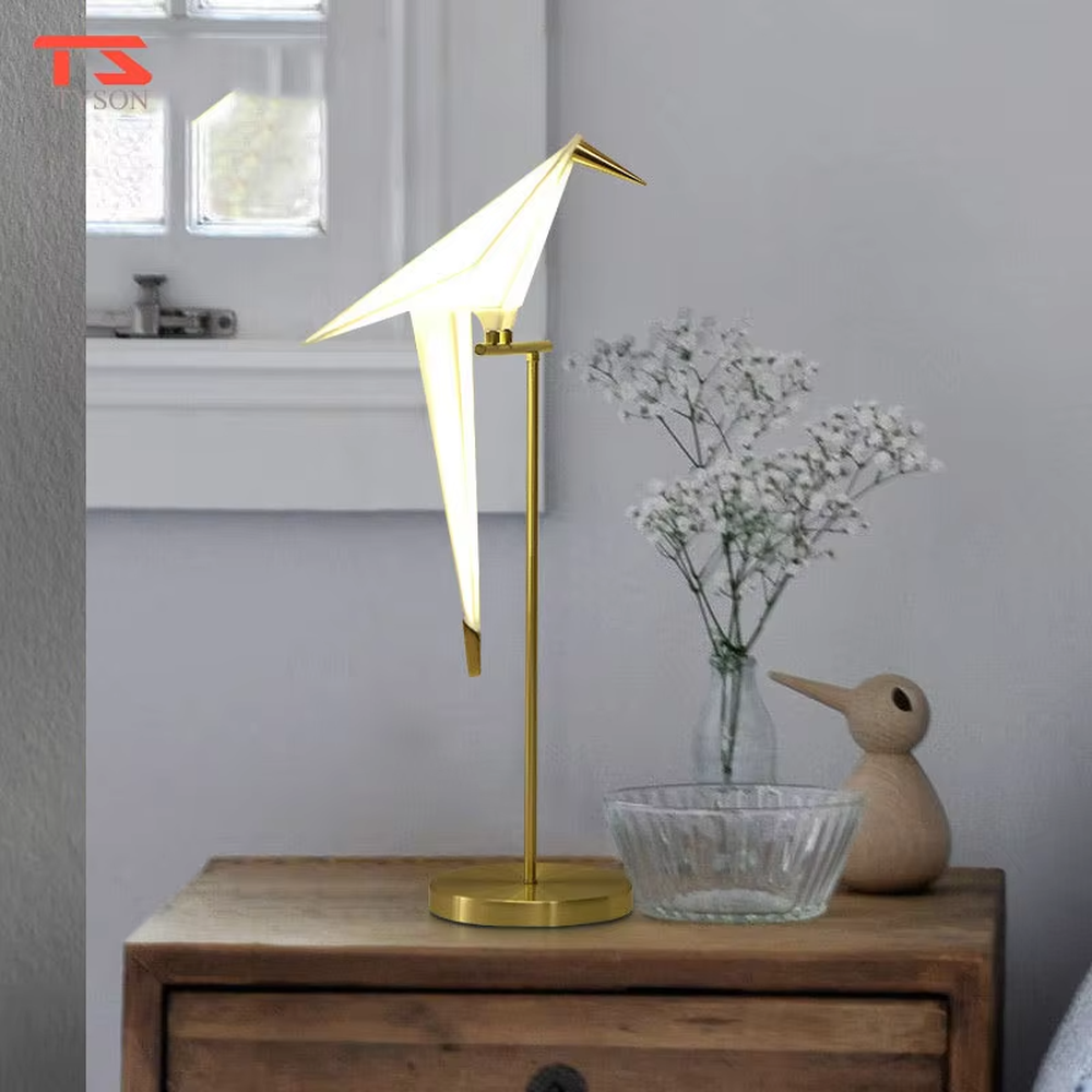 This is a modern light luxury origami crane-shaped table lamp, featuring a gold metal stand paired with a translucent paper art lamp body. The lamp body is as dynamic and soft as an origami crane, serving both lighting and artistic decoration purposes, suitable for bedroom nightstands, light luxury living room side tables, hotel guest rooms, showrooms and other scenarios.