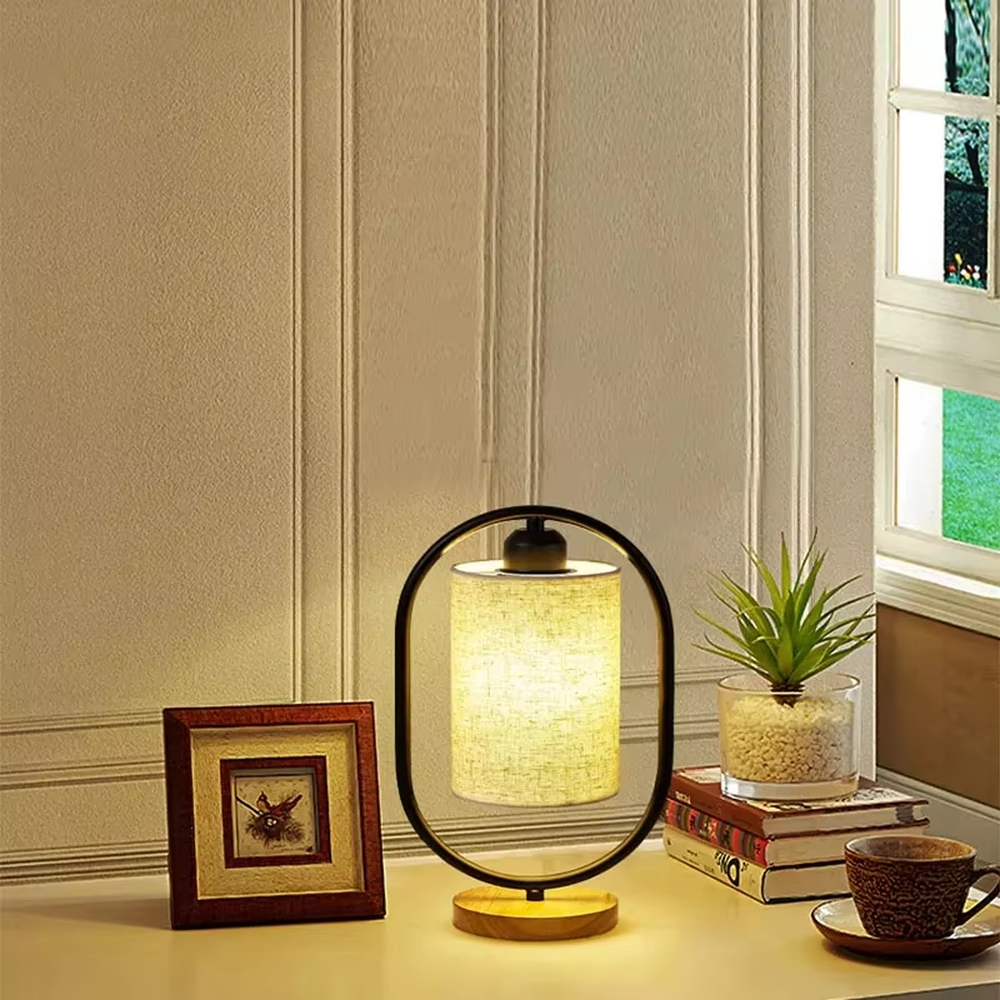 Modern minimalist silver oval metal frame linen texture lampshade wooden base table lamp, warm light effect, creating a cozy minimalist home atmosphere.