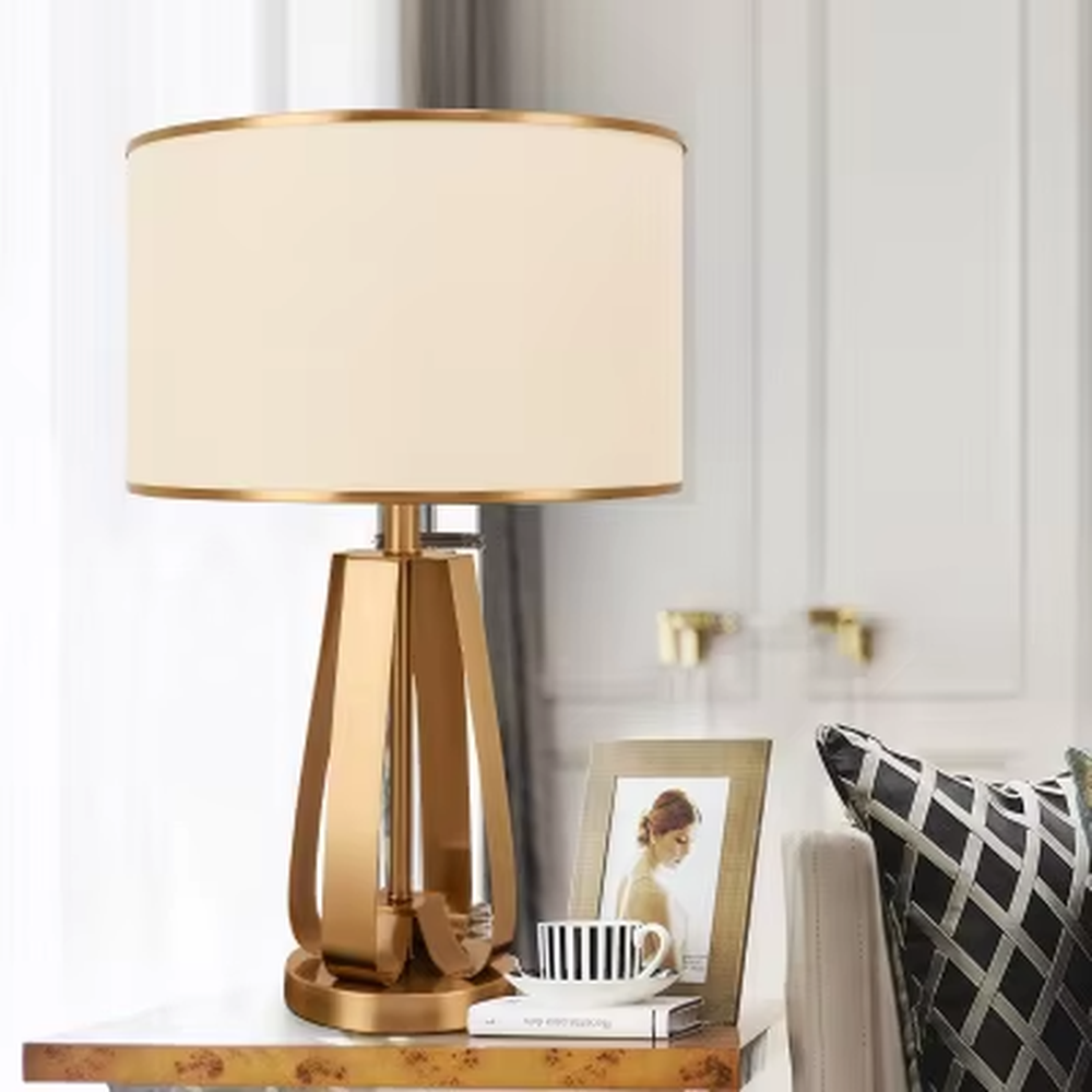 This is a light luxury geometric metal table lamp, featuring a gold polygonal hollow lamp base paired with an off-white fabric lampshade (with gold trim). It emits soft and warm light, serving both lighting and decorative purposes, suitable for bedroom nightstands, light luxury living room side tables, hotel guest rooms, showrooms and other scenarios.