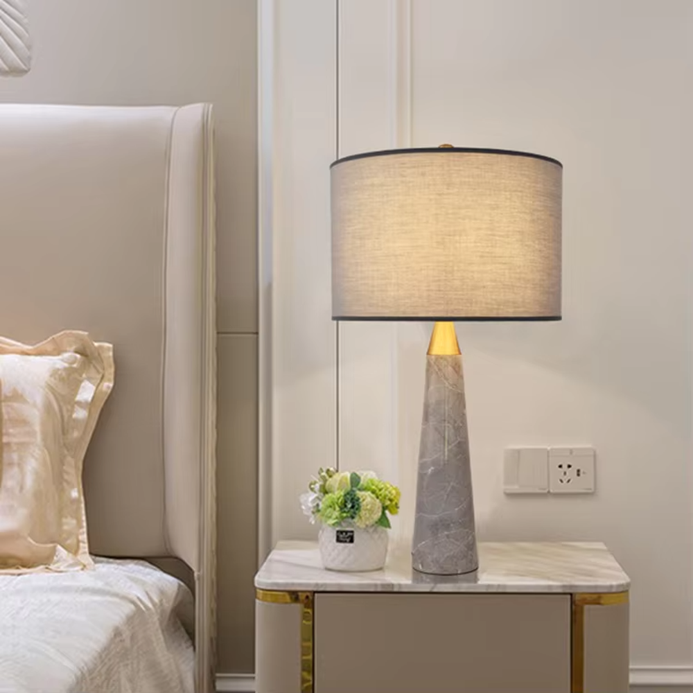 Light luxury marble cone table lamp, with a grey natural marble base, gold metal connection, off-white fabric lampshade with black trim, providing soft and warm light, designed to enhance the delicate texture of spaces, suitable for bedroom nightstands, living room side tables, modern light luxury homes and hotel guest rooms, etc.