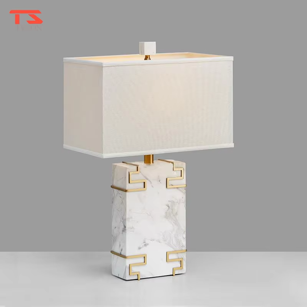 New Chinese light luxury style marble pattern table lamp, with a white faux marble lamp body paired with gold metal fretwork decoration, and a rectangular off-white fabric lampshade. It emits soft and elegant light, combining decorativeness and practicality, suitable for lighting and decoration in spaces such as bedroom nightstands, living room side tables, and New Chinese style show flats.