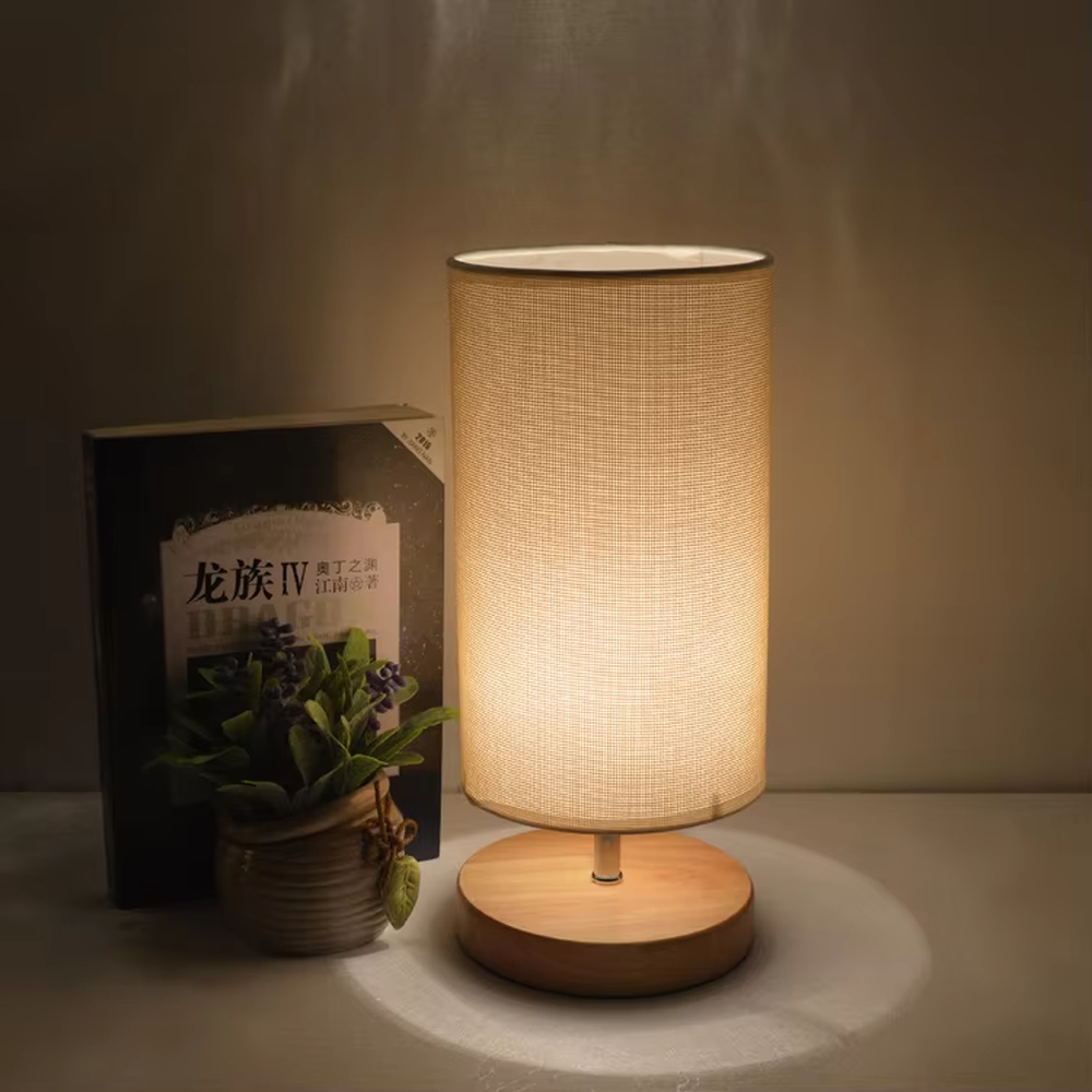 This is a minimalist square fabric table lamp, featuring a light beige linen lampshade paired with a black solid wood base. It emits soft and warm light, serving both lighting and decorative purposes, suitable for bedroom nightstands, desks, homestay guest rooms, living room side tables and other scenarios.