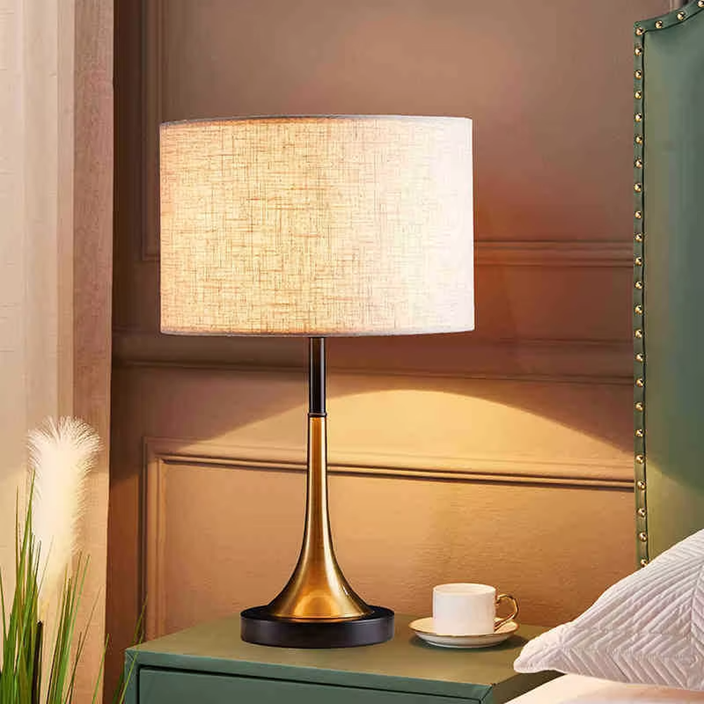 This modern light luxury table lamp features a black fabric cylindrical lampshade, paired with a black and gold contrasting metal lamp pole. The lower part is a trumpet-shaped gold metal design, and the base is black. The overall style is simple and elegant, with soft, non-glaring light, serving both lighting and decorative purposes, suitable for bedrooms, studies, living rooms and other spaces.
