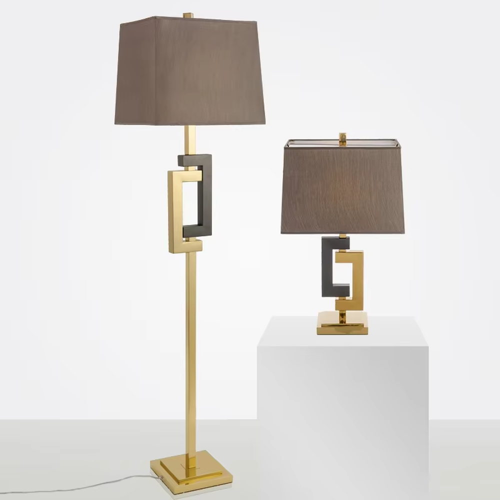This is a modern light luxury geometric interlocking table lamp, featuring an interlocking geometric lamp body crafted from gold and gray dual-color metal, paired with a dark gray fabric lampshade. It emits soft and uniform light, serving both lighting and decorative purposes, suitable for bedroom nightstands, light luxury living room side tables, hotel guest rooms, showrooms and other scenarios.