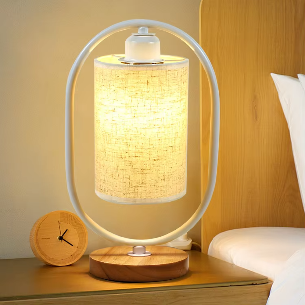 Modern minimalist silver oval metal frame linen texture lampshade wooden base table lamp, warm light effect, creating a cozy minimalist home atmosphere.