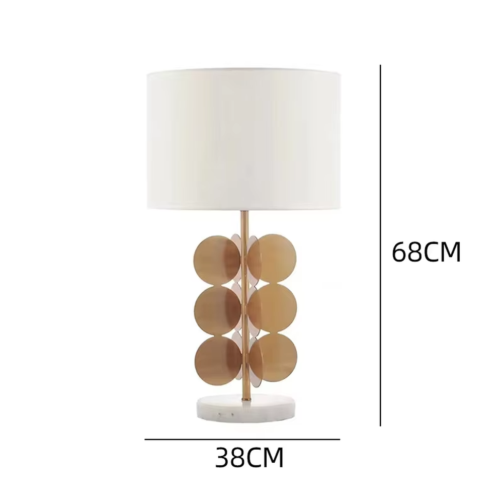 This light luxury table lamp features a white fabric cylindrical lampshade on top, a lamp post with a staggered stack of gold metal discs, and a white marble base, serving both lighting and decorative purposes, ideal for living room side tables, bedroom bedside tables, light luxury homestays and other spaces.