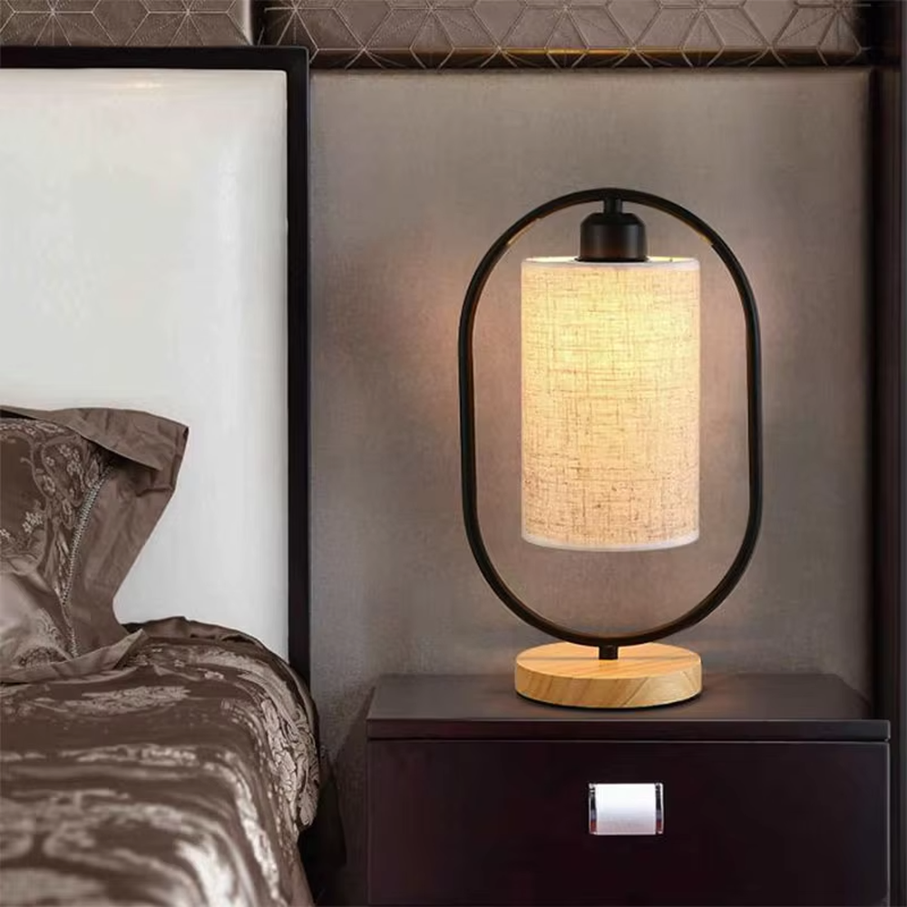 This is a modern minimalist oval frame table lamp, with a black metal oval stand paired with a beige linen lampshade and a solid wood base, featuring both decorative and lighting functions, ideal for warm indoor scenarios such as bedroom nightstands and living room side tables.
