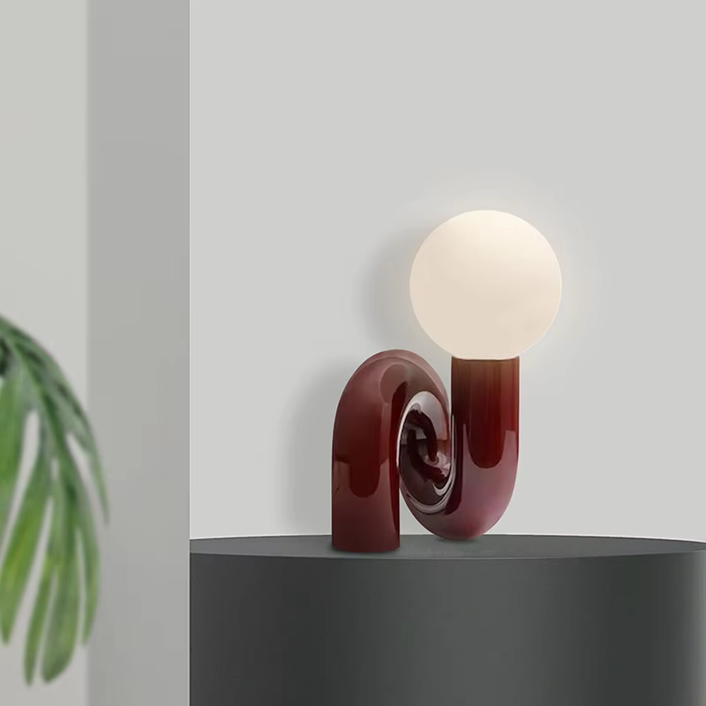This art table lamp features a spiral S-shaped stand made of glossy wine-red material, paired with a milky white spherical lampshade, with a vivid and retro shape, serving both lighting and decorative purposes, ideal for bedrooms, living rooms, internet-famous shops and other spaces.