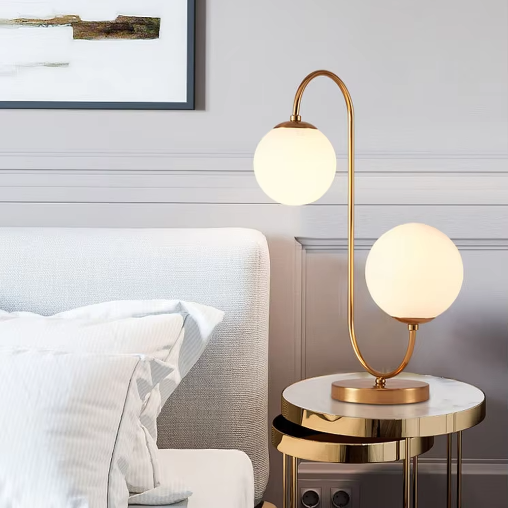Light luxury double-ball curved table lamp (gold metal curved bracket + double milk-white glass ball lampshades + round metal base), warm light effect, creating a modern and elegant home atmosphere.