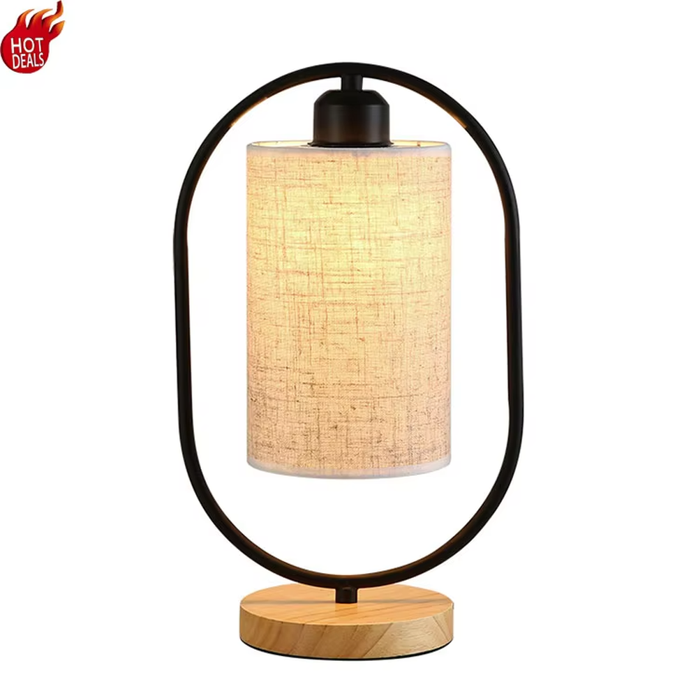 This is a modern minimalist oval frame table lamp, with a black metal oval stand paired with a beige linen lampshade and a solid wood base, featuring both decorative and lighting functions, ideal for warm indoor scenarios such as bedroom nightstands and living room side tables.