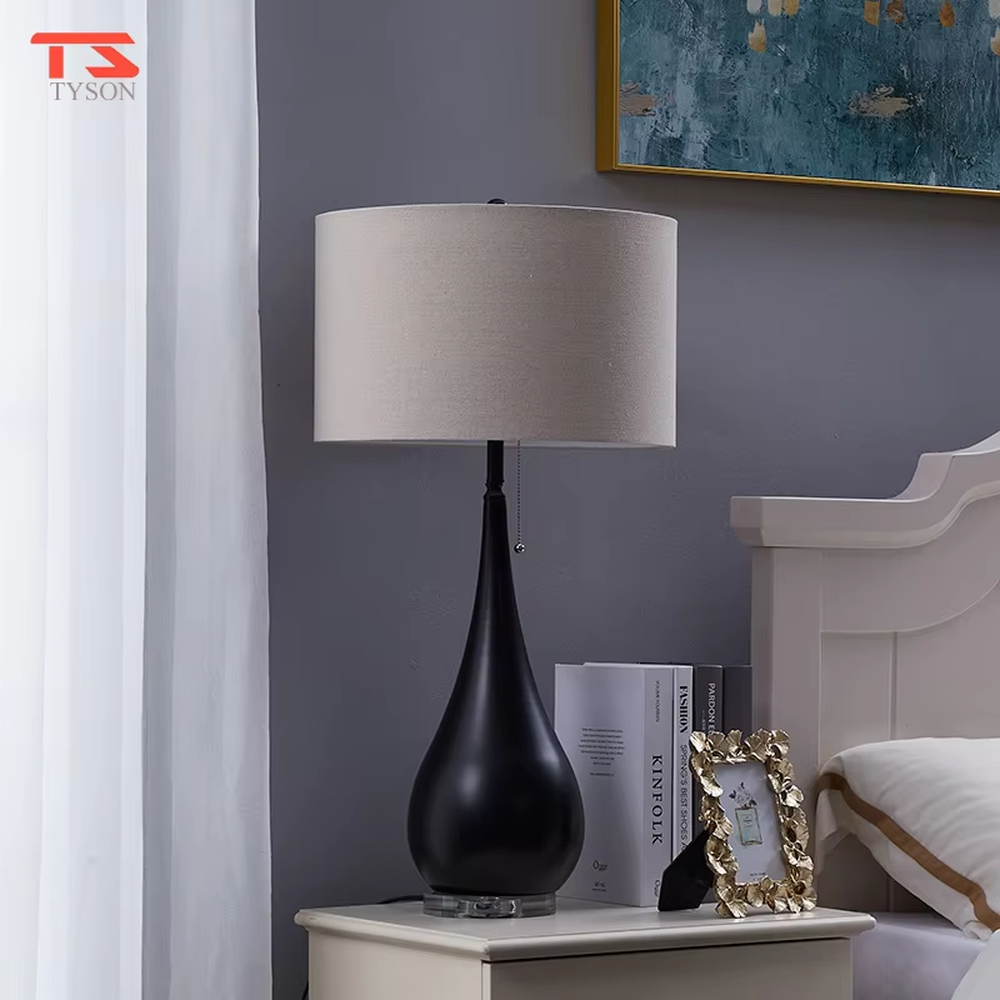 This is a pastoral-style floral fabric table lamp, with an off-white lampshade printed with blue and black floral patterns, paired with a black matte teardrop-shaped base and transparent crystal feet, featuring both decorative and lighting functions, ideal for warm indoor scenarios such as bedroom nightstands and living room side tables.