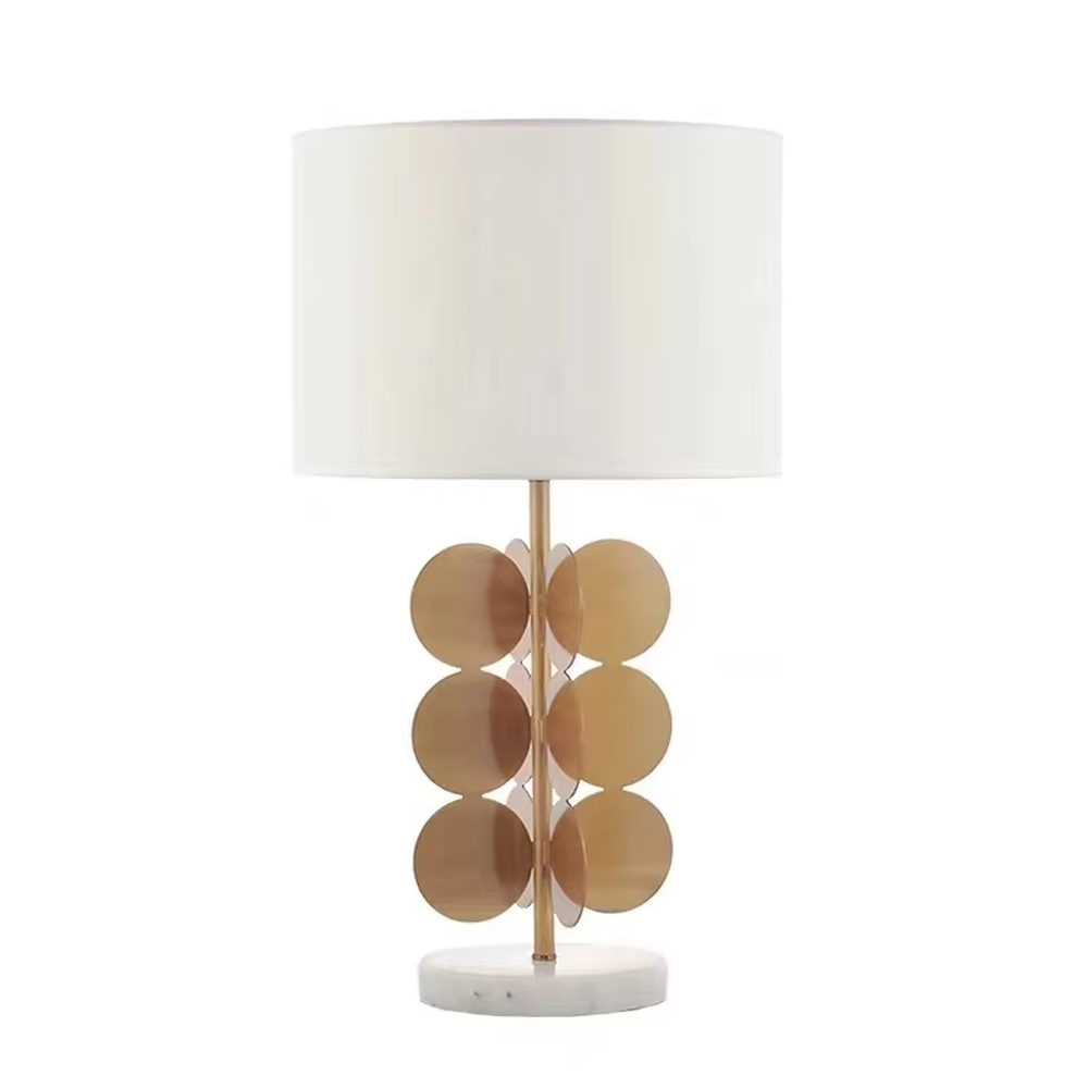 This light luxury table lamp features a white fabric cylindrical lampshade on top, a lamp post with a staggered stack of gold metal discs, and a white marble base, serving both lighting and decorative purposes, ideal for living room side tables, bedroom bedside tables, light luxury homestays and other spaces.