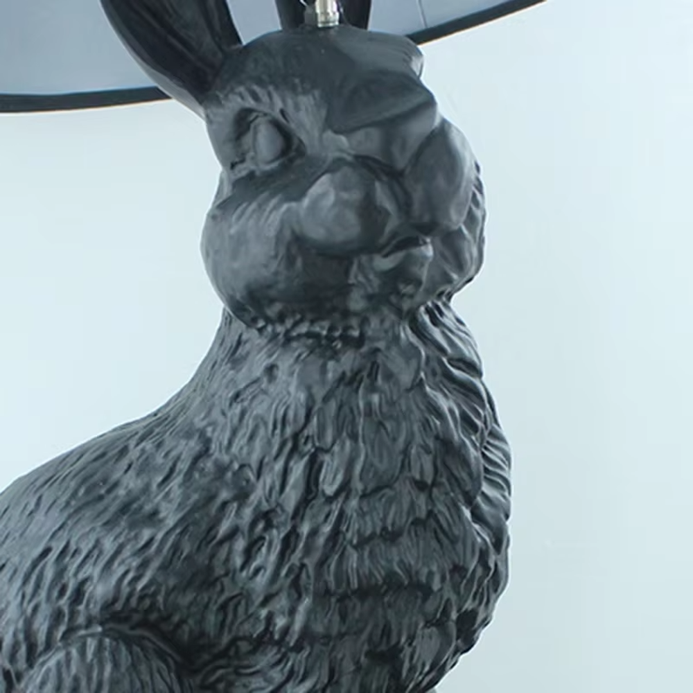 This dark art style table lamp features a bionic rabbit-shaped base made of black resin, paired with a black fabric cylindrical lampshade. The rabbit-lifting-lampshade design is full of fantasy, serving both lighting and decorative purposes, ideal for trendy toy spaces, personalized homes, internet-famous shops and other scenarios.