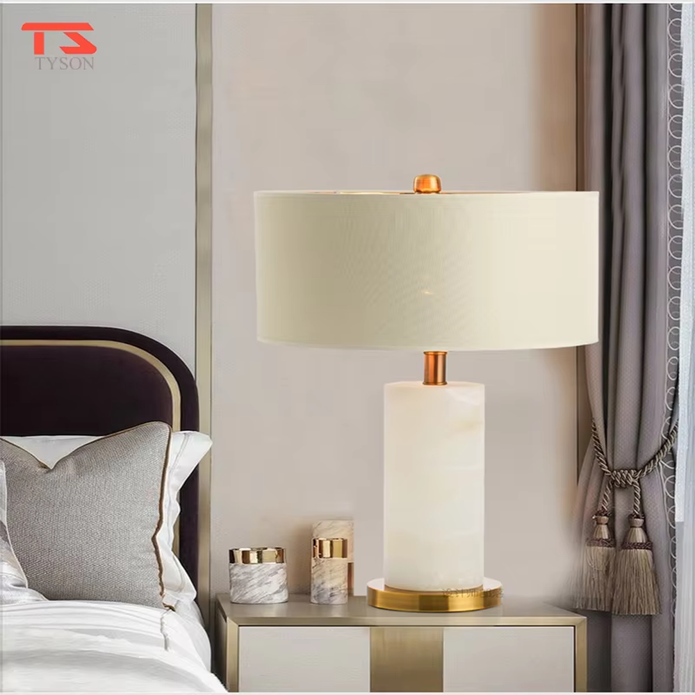 This is a light luxury minimalist table lamp, featuring a natural marble lamp post paired with gold metal accents and an off-white fabric lampshade. It emits soft and gentle light, serving both lighting and decorative purposes, suitable for bedroom nightstands, hotel guest rooms, light luxury living room side tables, showrooms and other scenarios.