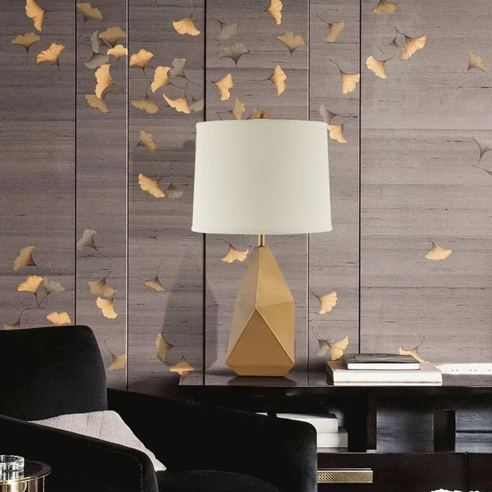 Modern light luxury style geometric cut metal table lamp, featuring a gold rhombus lamp body paired with an off-white fabric lampshade (with a gold trim at the bottom), designed for both tabletop placement and hanging. It emits soft and warm light, combining decorativeness and practicality, suitable for lighting and decoration in spaces such as living room side tables, bedroom nightstands, and hotel guest rooms.