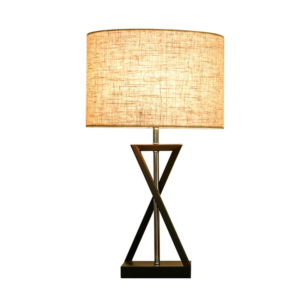 This is a modern minimalist fabric table lamp, featuring an off-white linen lampshade paired with a geometric cross-shaped white and silver dual-color lamp base, which has both lighting and decorative functions, suitable for bedroom nightstands, study desks, hotel guest rooms and other spaces.