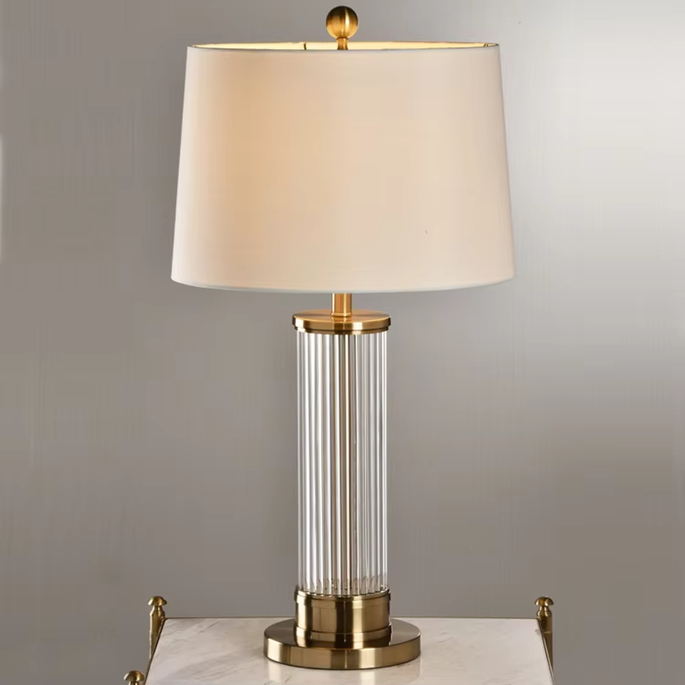 This is a light luxury crystal metal table lamp, with an off-white fabric lampshade edged with gold trim, a lamp post made of vertical striped transparent crystal paired with gold metal splicing, and a gold metal base, featuring both decorative and lighting functions, ideal for high-end indoor scenarios such as bedroom nightstands and living room side tables.