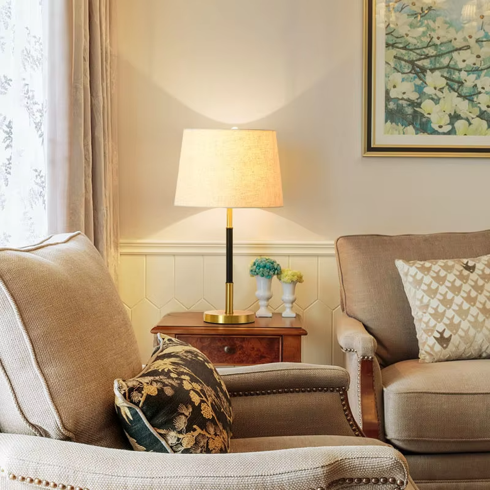 This is a minimalist light luxury table lamp, featuring an off-white linen fabric lampshade paired with a black and gold dual-color metal lamp pole, with a pull-chain switch. It emits soft and warm light, serving both lighting and decorative purposes, suitable for bedroom nightstands, living room side tables, studies, hotel guest rooms and other scenarios.