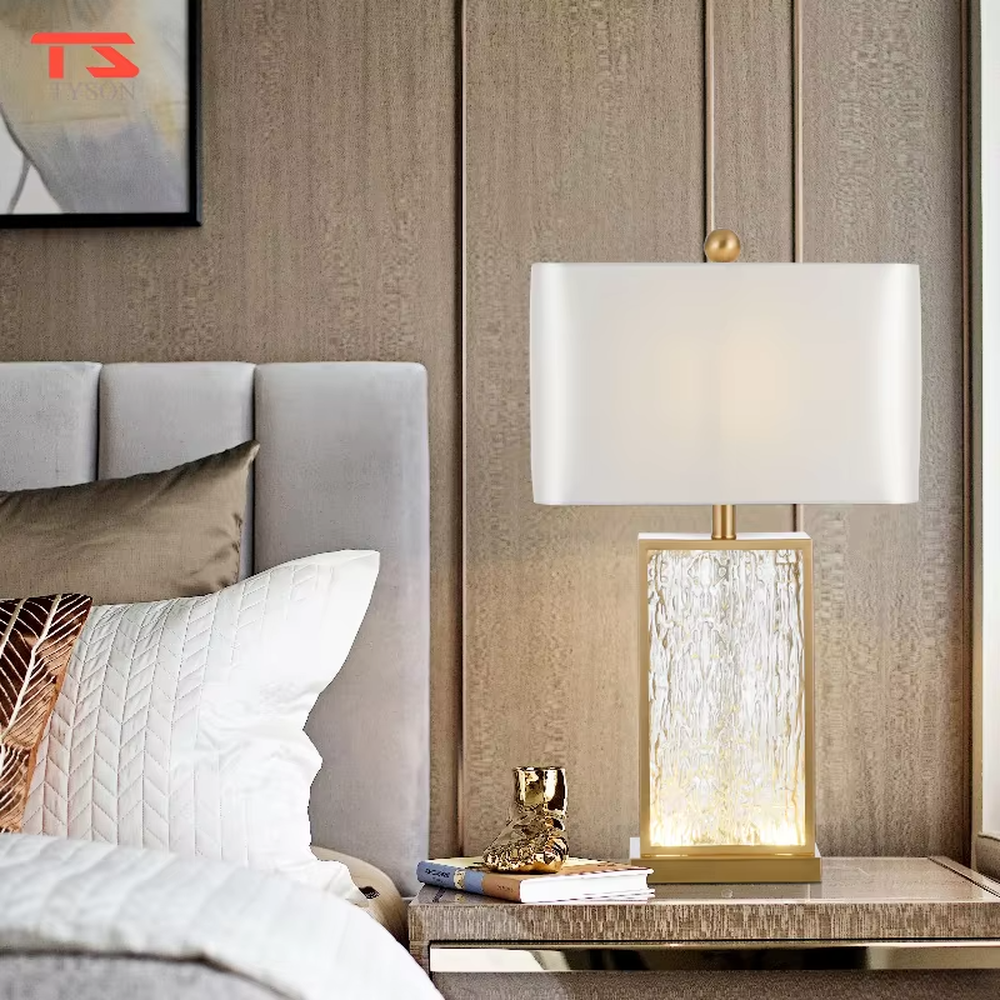 This modern light luxury table lamp features a gold metal frame, paired with a water-textured transparent glass lamp body and a white fabric rectangular lampshade. It serves both lighting and decorative purposes, ideal for light luxury spaces such as bedroom bedside tables, living room side tables, and hotel guest rooms.
