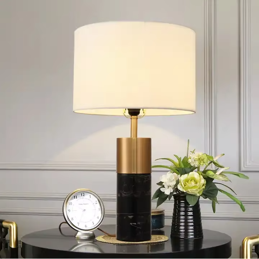This light luxury modern table lamp features a lamp post made of black marble and gold metal, paired with an off-white fabric cylindrical lampshade. It has a calm and elegant shape, serves both lighting and decorative purposes, and is ideal for bedroom bedside tables, living room side tables, hotel guest rooms and light luxury commercial spaces.