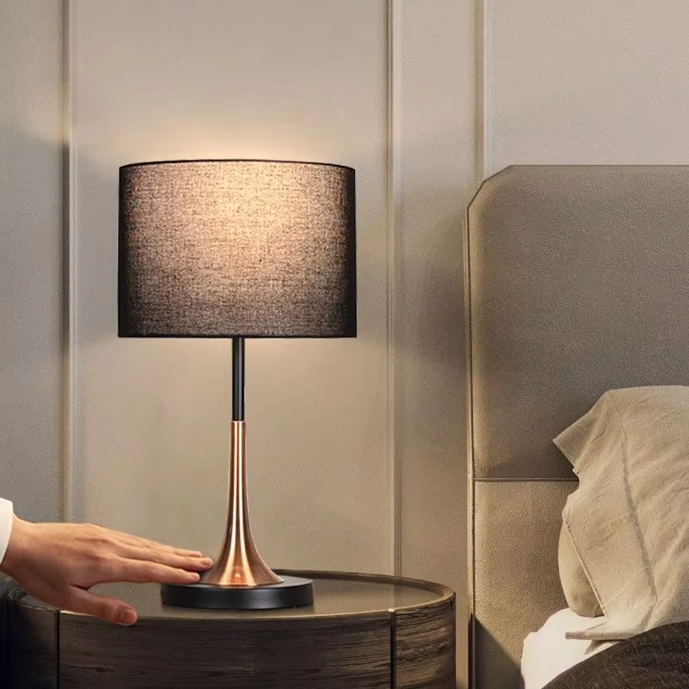 This modern light luxury table lamp features a black fabric cylindrical lampshade, paired with a black and gold contrasting metal lamp pole. The lower part is a trumpet-shaped gold metal design, and the base is black. The overall style is simple and elegant, with soft, non-glaring light, serving both lighting and decorative purposes, suitable for bedrooms, studies, living rooms and other spaces.
