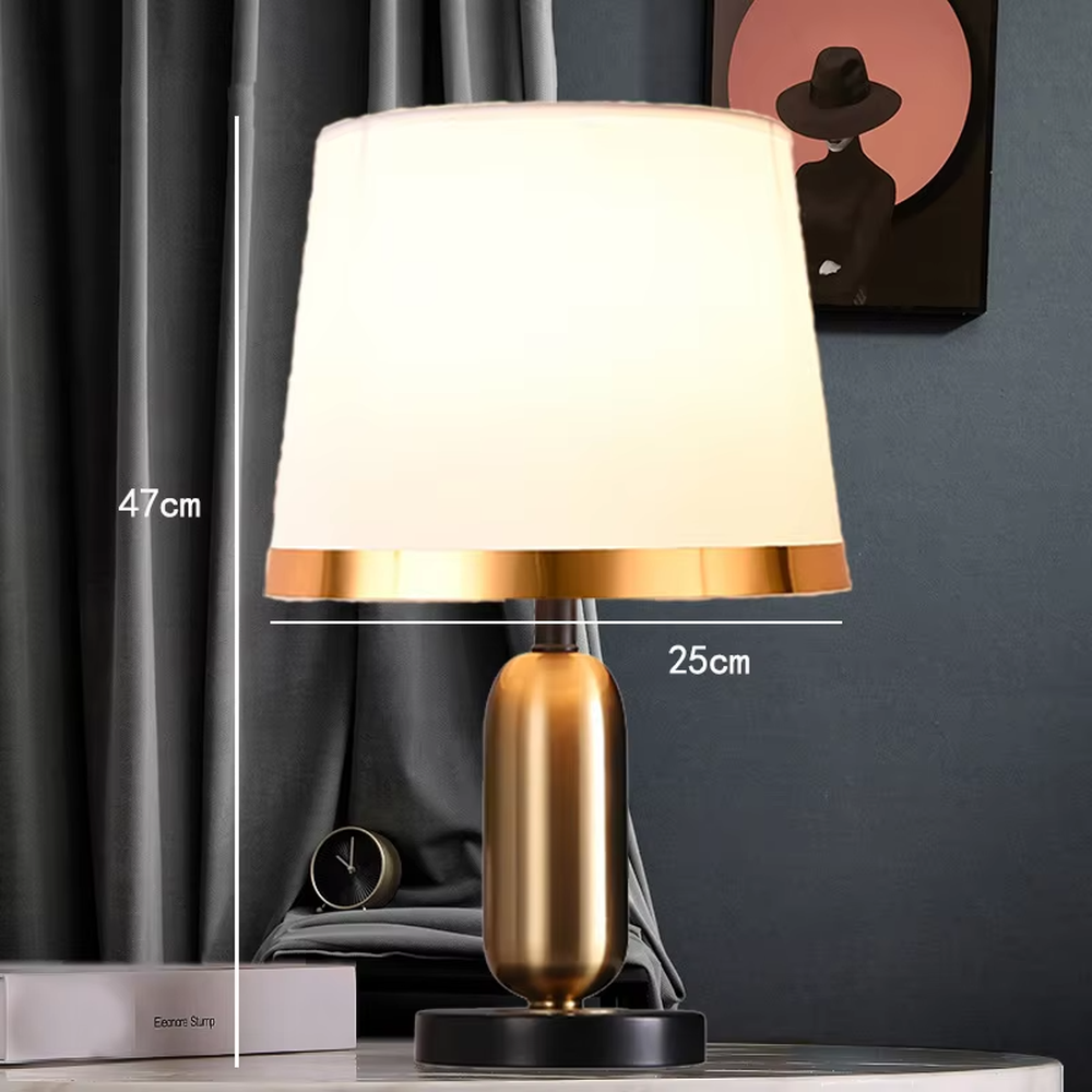 This is a light luxury minimalist style table lamp, featuring a gold metal lamp body paired with an off-white fabric lampshade. The black and gold color scheme offers a high-end texture, emitting soft and uniform light, serving both lighting and decorative purposes, suitable for bedroom nightstands, hotel guest rooms, light luxury living room side tables and other scenarios.