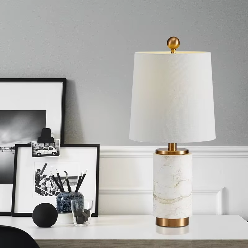 Light luxury white marble cylindrical table lamp, white marble base + golden metal decorations + beige fabric lampshade, soft warm light, creating an elegant light luxury home atmosphere.