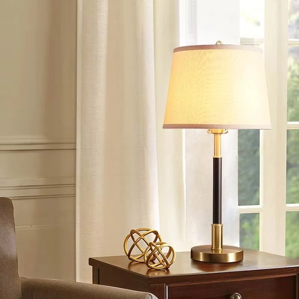 This table lamp features a black and gold contrasting metal lamp pole paired with an off-white fabric lampshade, with a glossy gold metal base. It presents a style that combines modern light luxury and minimalist retro, with soft eye-protective light, serving both lighting and decorative purposes, suitable for placement in bedrooms, studies and other spaces.