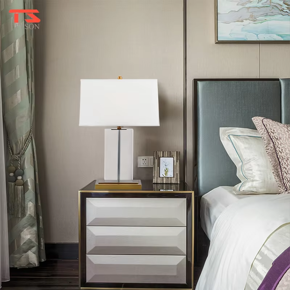 This modern light luxury table lamp features an off-white fabric lampshade (trimmed with a thin gold edge), paired with a transparent crystal square column lamp pole and a gold metal base. The overall style is simple and elegant, with soft eye-protective light, serving both lighting and decorative purposes, suitable for modern light luxury style spaces such as bedrooms, living rooms, and hotel guest rooms.