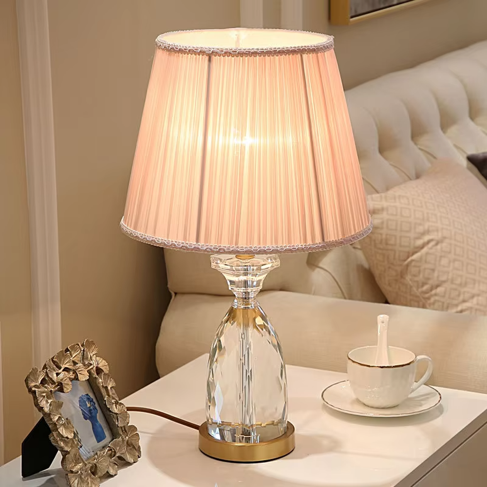 Light luxury crystal table lamp, with a diamond-cut crystal base, pink pleated fabric lampshade and gold metal details, providing soft and warm light, designed to enhance the elegant atmosphere of spaces, suitable for bedroom nightstands, living room side tables, princess rooms, etc.